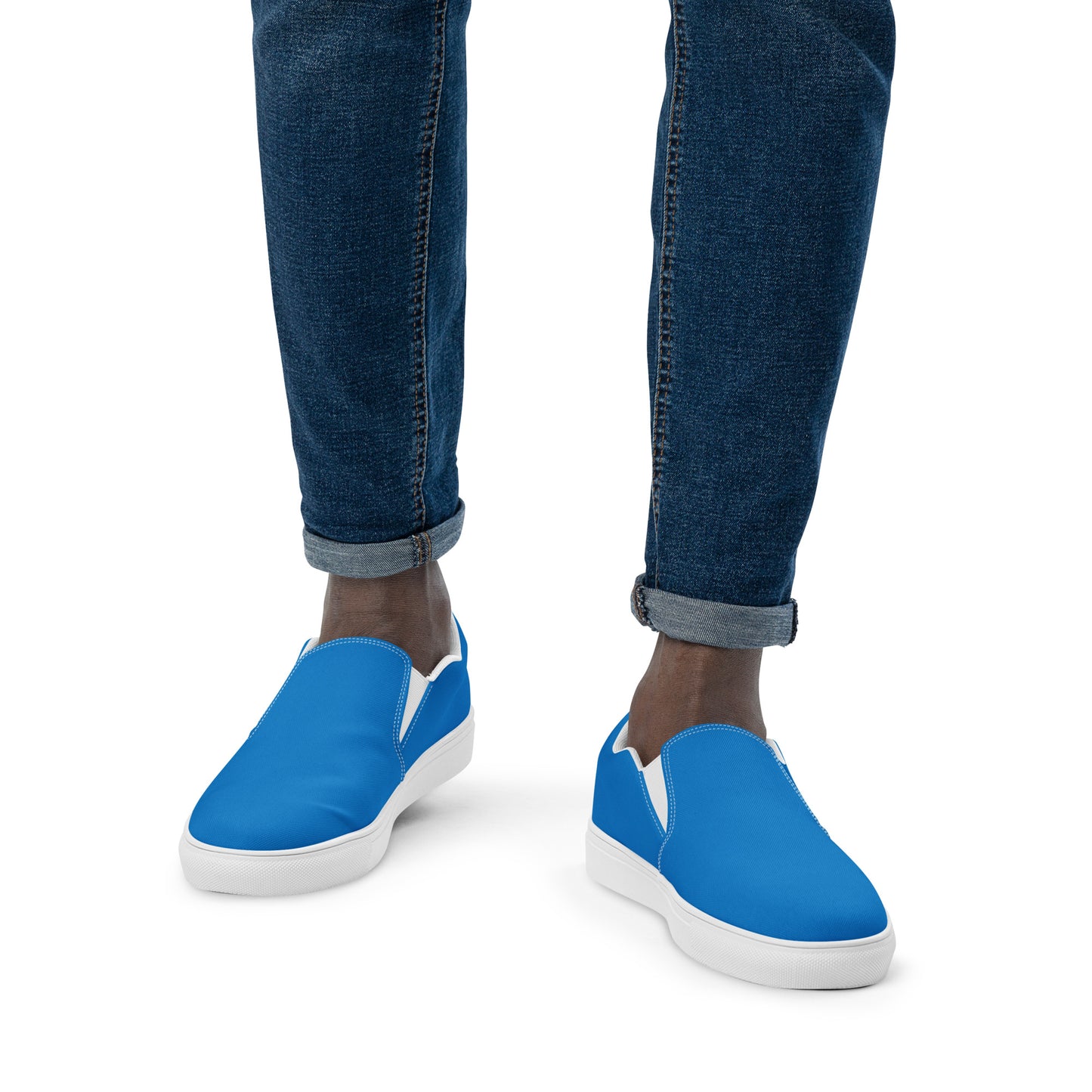 Blue slip-on shoes with white soles worn with rolled-up jeans on a white background