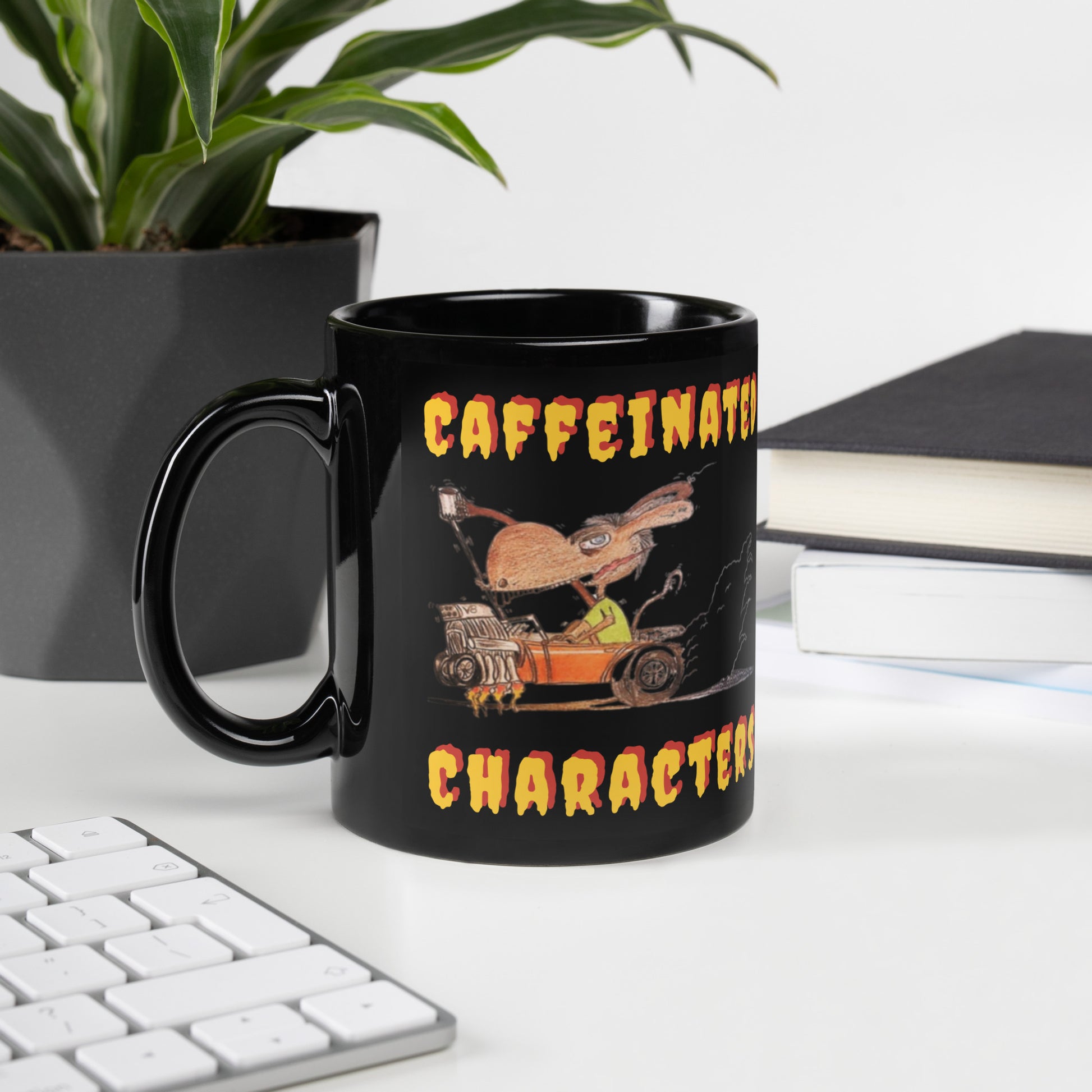 Caffeinated-CharacterYellow-and-Orange-black-glossy-mug-11-oz-handle-on-left side sitting on a white desk next to a plant, keyboard and some books