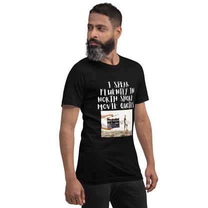 I speak in North Shore Movie Quotes in large text, Picture of a Movie Scene Marker with Surfer holding a surfboard on the beach short sleeve t-shirt in black, side view